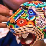 Artesana realizando arte huichol con una figura de un jaguar hecha de chaquira