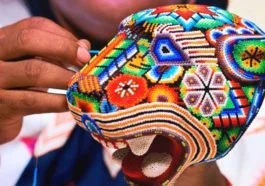 Artesana realizando arte huichol con una figura de un jaguar hecha de chaquira