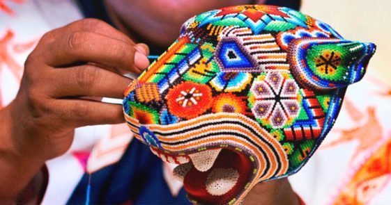 Artesana realizando arte huichol con una figura de un jaguar hecha de chaquira