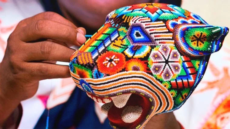 Artesana realizando arte huichol con una figura de un jaguar hecha de chaquira
